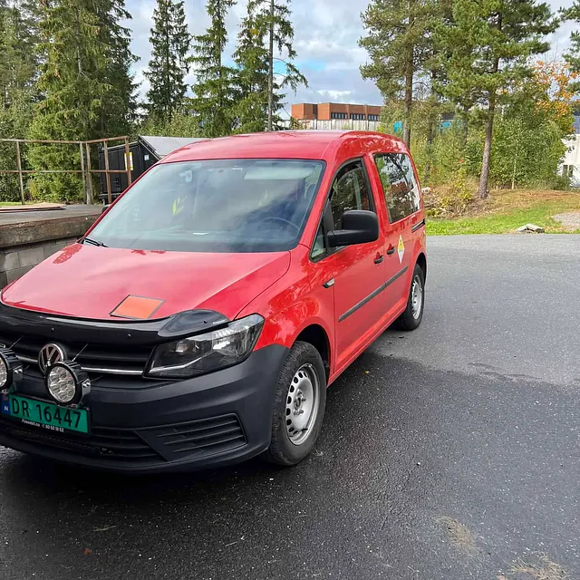 Rød varebil parkert på våt asfalt med trær og bygninger i bakgrunnen.