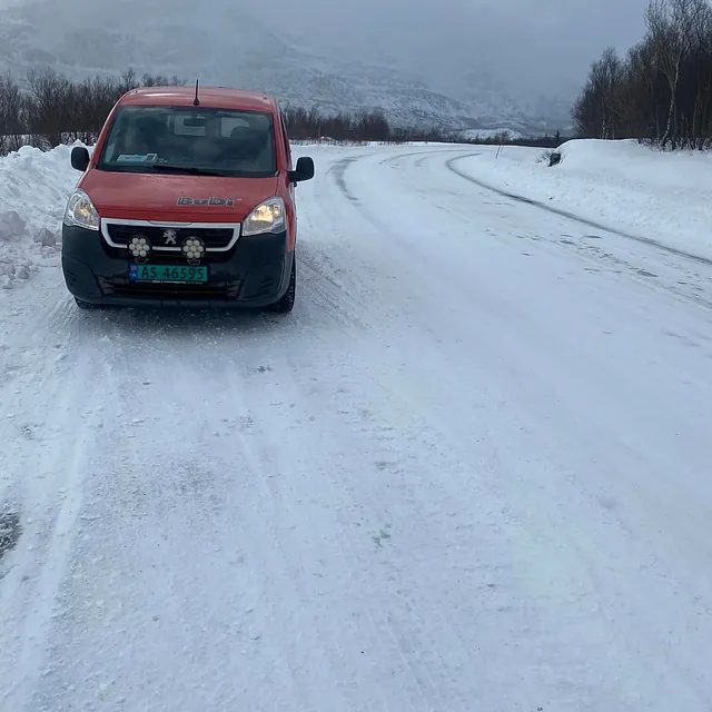 Rød varebil står på snødekt vei i vinterlandskap med fjell og skog rundt.