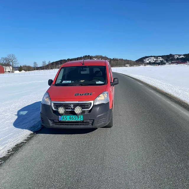 Rød varebil parkert langs landevei med snødekte jorder og klar blå himmel.