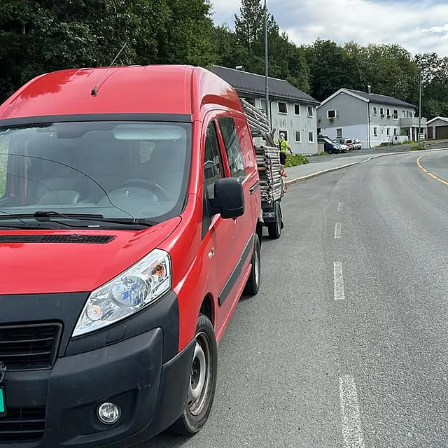Rød varebil med lastet tilhenger parkert langs vei i boligområde.