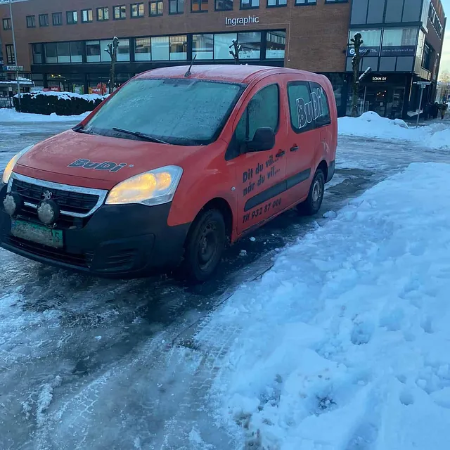 Rød varebil parkert på isete gate foran kontorbygg med snø langs fortauet.